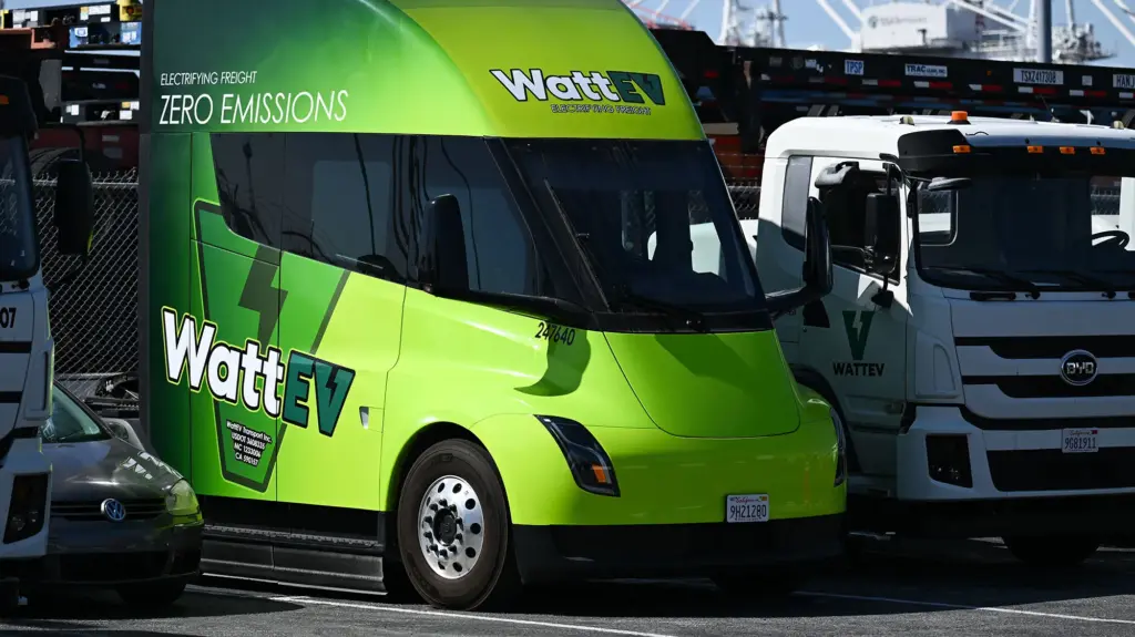 A bright green, privately branded Tesla big rig sits in a parking spot on a sunny day.