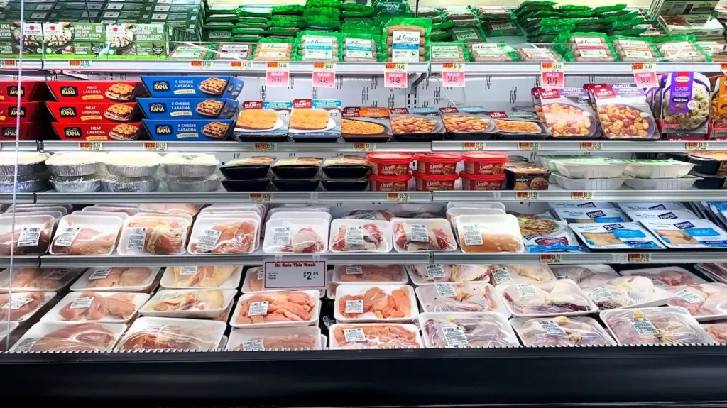 Frozen and refrigerated foods, like raw chicken and other meats, in a grocery store.