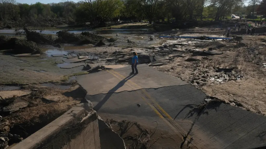 A person stands at the end of a road bridge, parts of which were swept away by floodwaters.