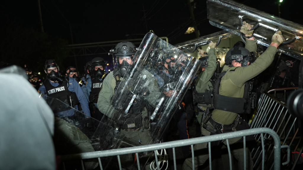 Several enforcement officers, some in green suits and some in blue suits with tactical gear labeled