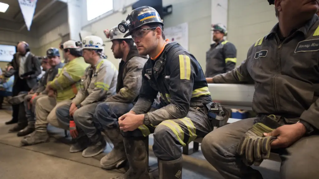 Coal miners sit along a bench in dusty coveralls and jackets. The miners are white, mostly young, men.