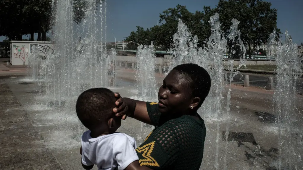 An African woman and her child in Lyon cool off by a public fountain on a sweltering day