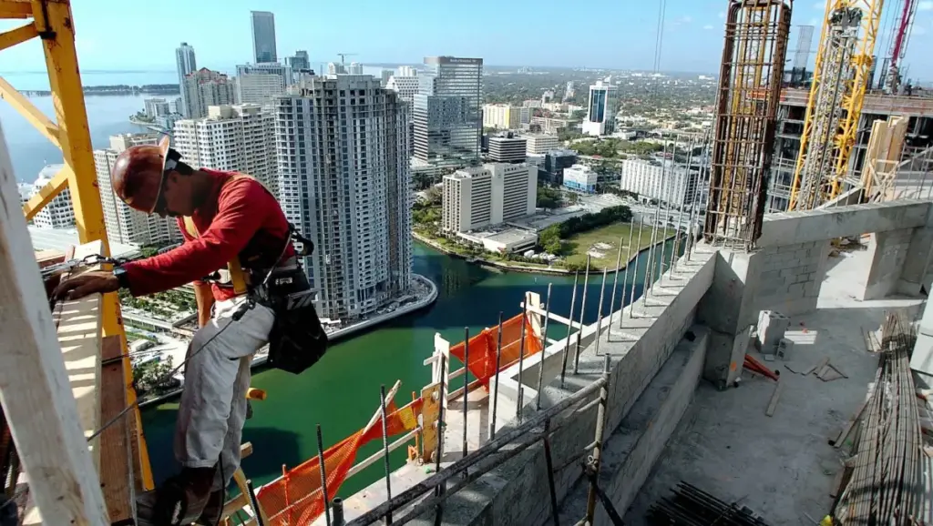 a construction worker in an orange helmet climes on a tower atop a tall building under construction