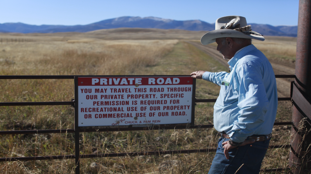 Man stands in front of a gate that prohibits people from entering private property.