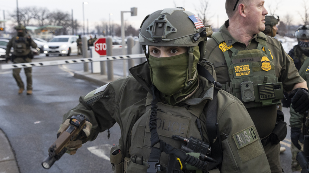 a masked border patrol agent holds a gun