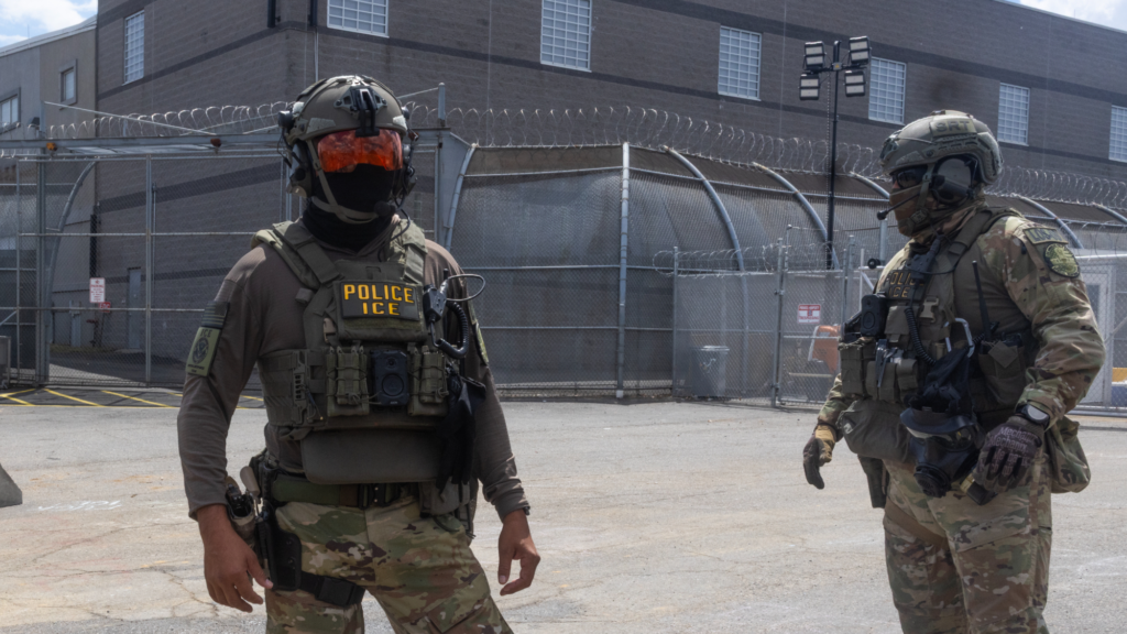 two armed ice agents stand outside delaney hall in new jersey.
