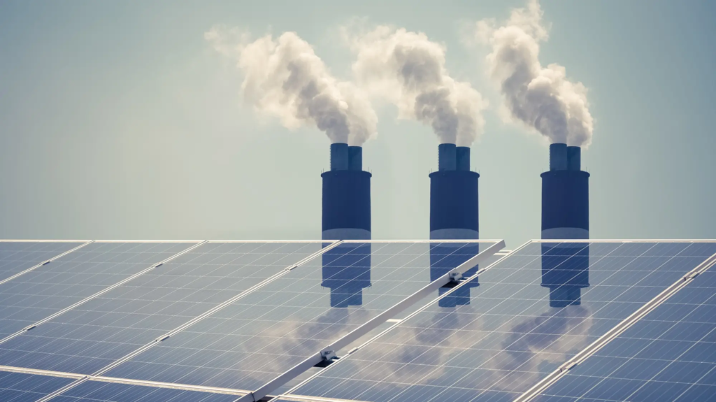 Solar panels in front three coal plant smoke stacks.