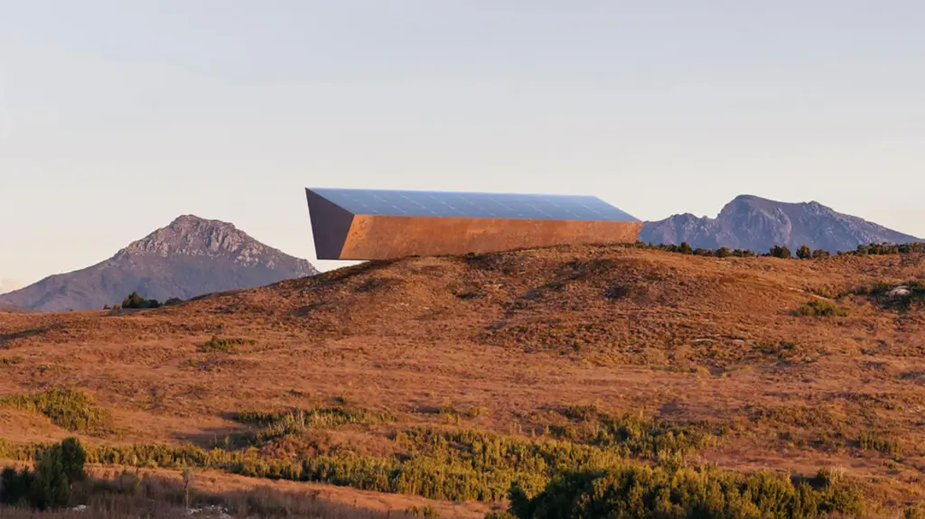 A long, futuristic looking, steel structure sits atop an arid hill.