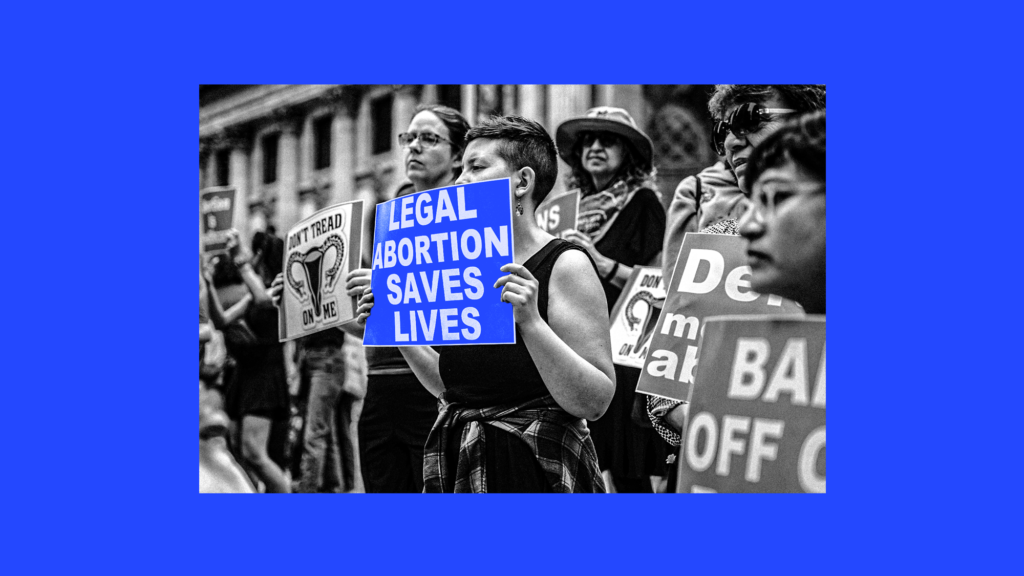 A photo illustration of a black-and-white photo with a woman in a dress standing in a crowd holding a blue sign that reads