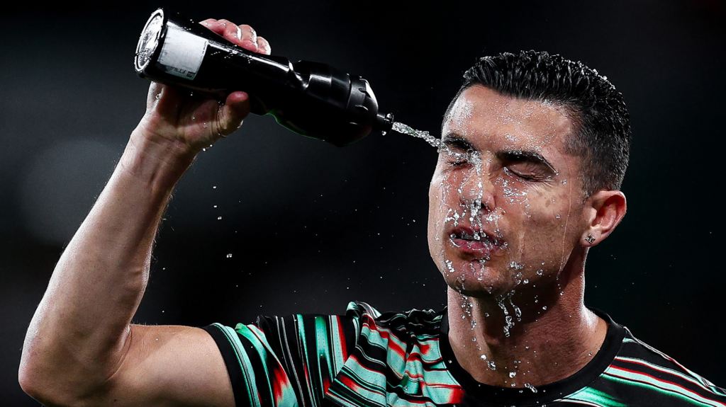 Man squirts water onto his face from black water bottle.