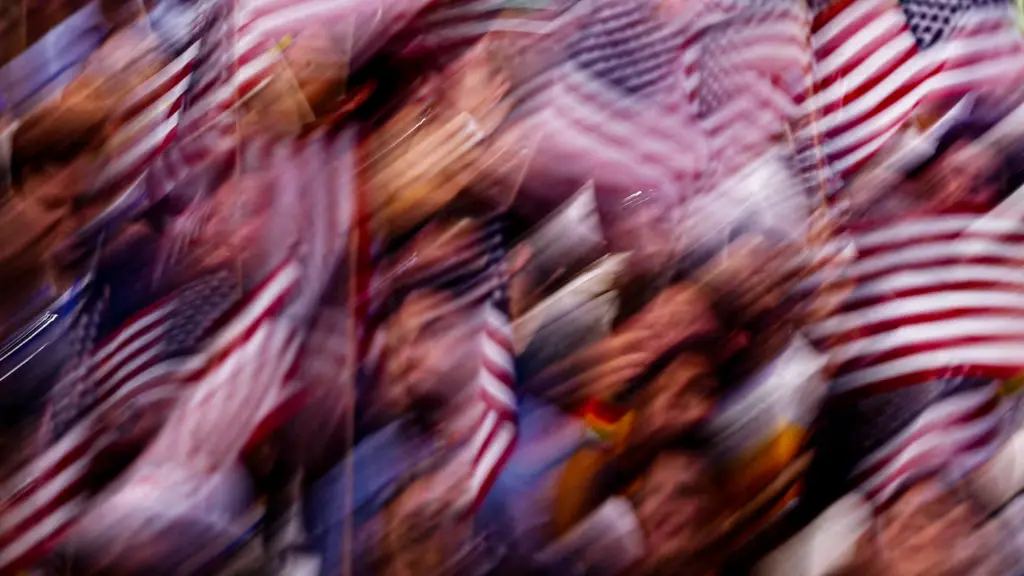 A motion-blurred photo of a crowd of people waving small American flags.