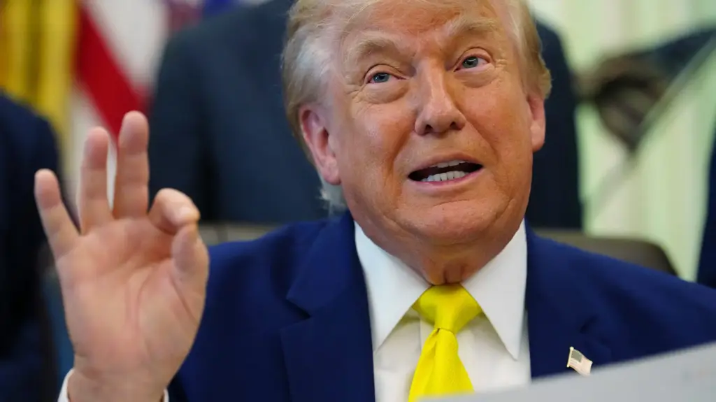 Tight photo of Donald Trump in a navy suit and yellow tie with his hand making something like the A-OK sign