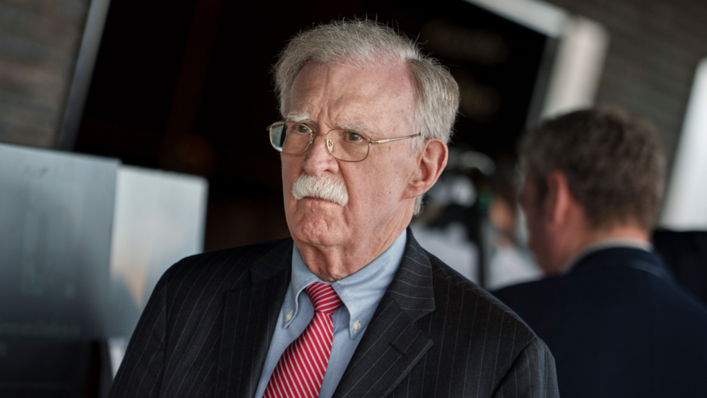A photo of former Trump national security adviser John Bolton facing forward with his body angled slightly toward the viewer's left. He is wearing a suit and glasses.
