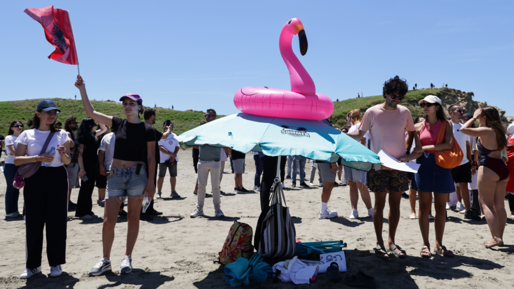 A woman waves an albanian flag next to an inflated flamingo.