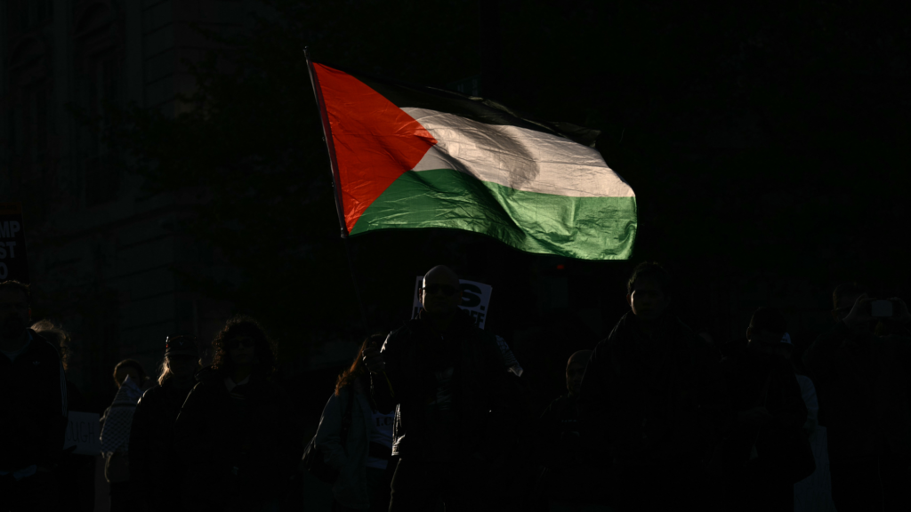 A Palestinian flag waves above a protest at night.