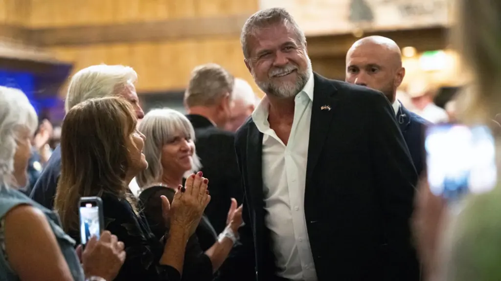Marx in a dark suit and white button-down shirt, open at the collar, smiling in a crowd of supporters