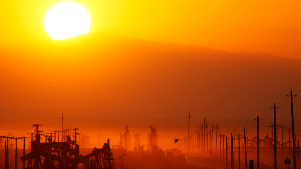 The sun rises over an oil field in an orange glow.