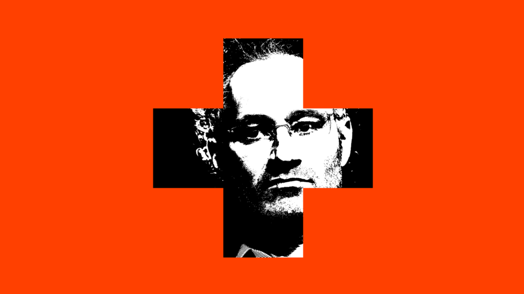 A photo illustration of the CEO of Palantir, Alex Karp, peeking through a cross-shaped hole in a red wall. Karp is an upper middle-aged man with graying curls of hair. He also wears thin-framed rectangular glasses.