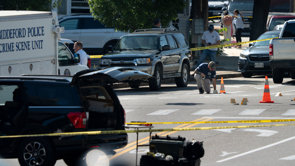 Yellow crime scene tape crosses an intersection with multiple cars and a white cargo van that says