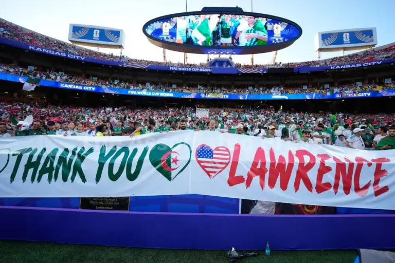 Thousands of fans are seen in the distance at a World Cup stadium in Kansas City. The fans in the front are holding a giant banner that says