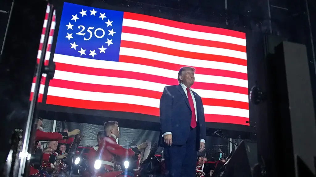 Donald Trump standing in front of a big, electronice American Flag.