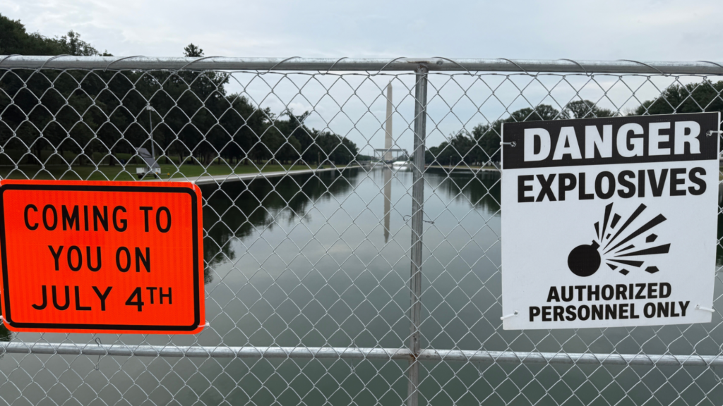 A photo of a fence with two signs. One is orange and says