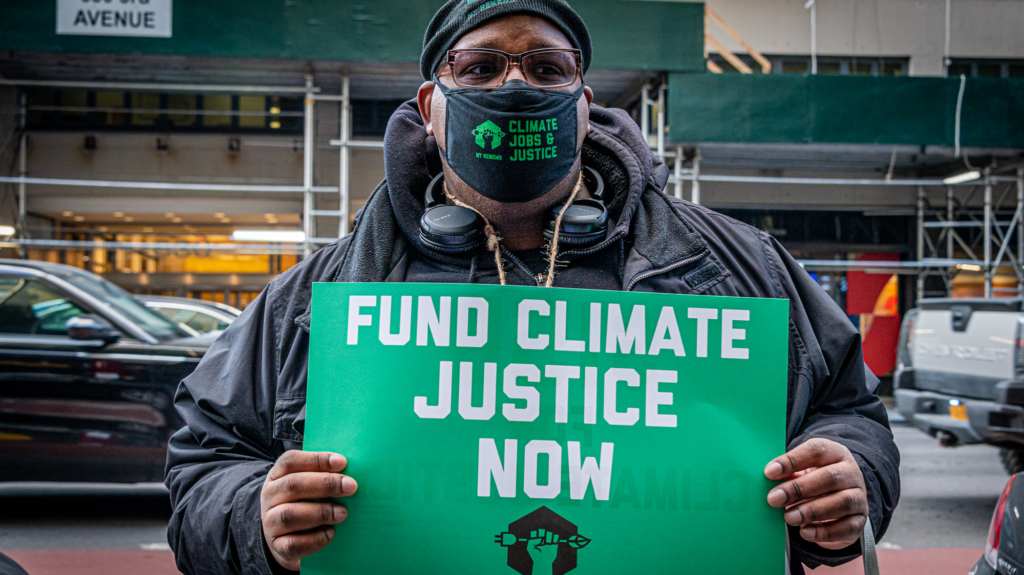 A man with a face mask holds a green sign that reads, 