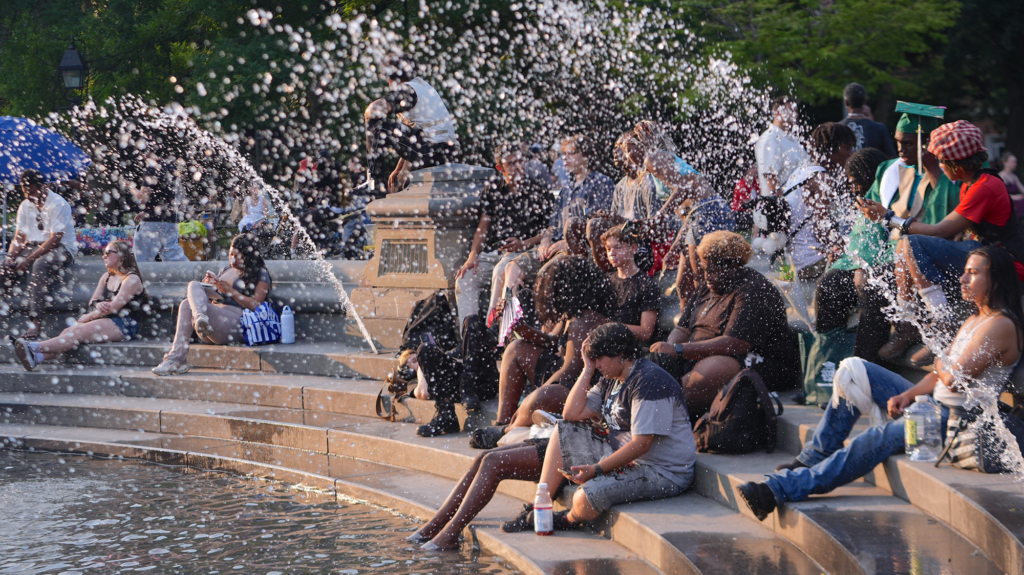 People gather to sit in a fountain and are sprayed by water.