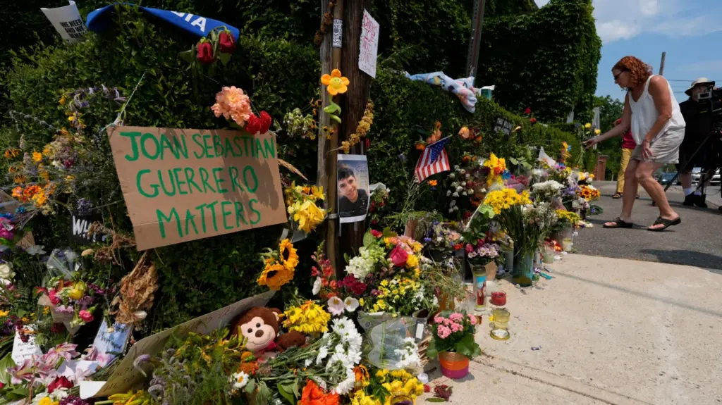 A woman in a white blouse and shorts leans to place flowers in a memorial.