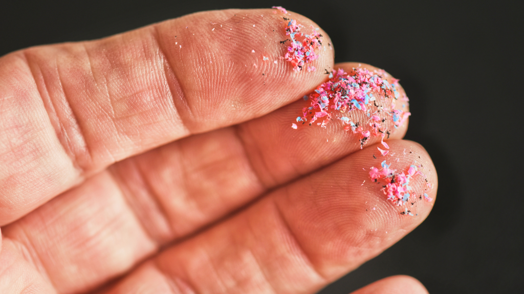 Small colorful plastic particles lie on someone's fingers.