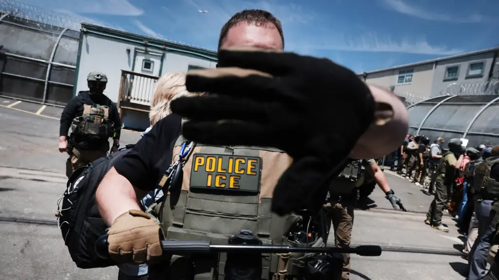 An ICE agent holds his hand up to the camera obscuring the view of the photographer; he holds a baton in his opposite hand.