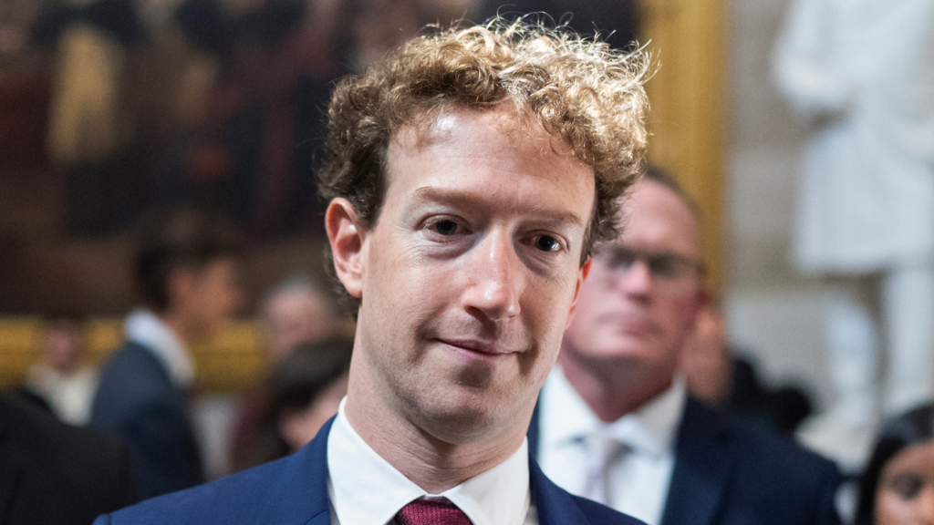 Mark Zuckerberg's face and shoulders are shown. His brown hair is slightly messy and he stares with a blank expression. Several people in formal dress are in the background.