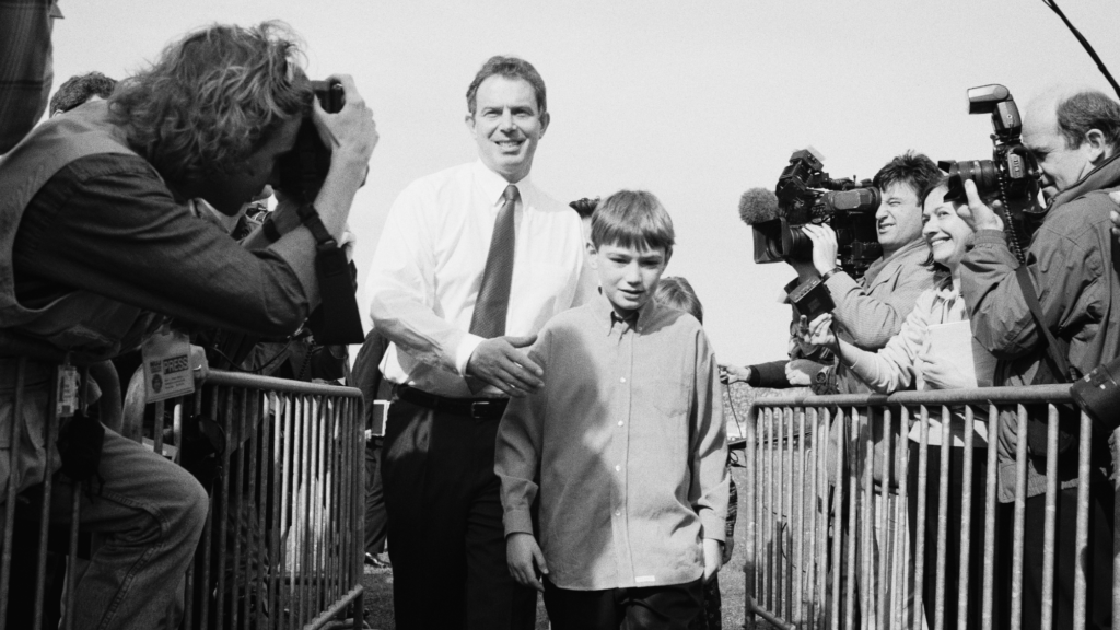 A black-and-white photo of Tony Blair campaigning with his son, Nick Blair, who is in this instance a child. It is 1997.