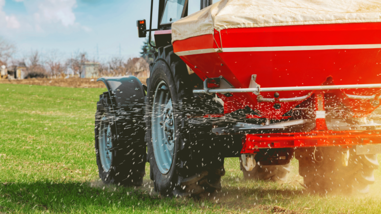 A red farm vehicle spreads NPK fertilizer, which contains nitrogen, phosphorus, and potassium.
