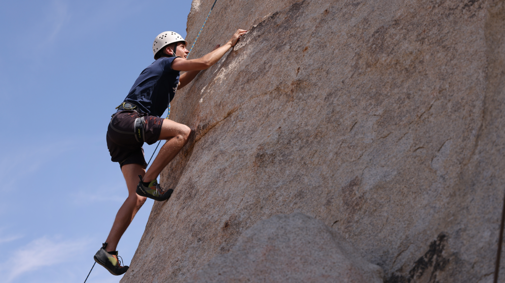 A man with a white helmet climbs up a rock using a rope.