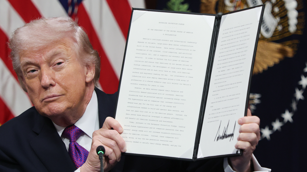 Trump peers to the side of a folded white paper with writing. An American flag hangs in the background.