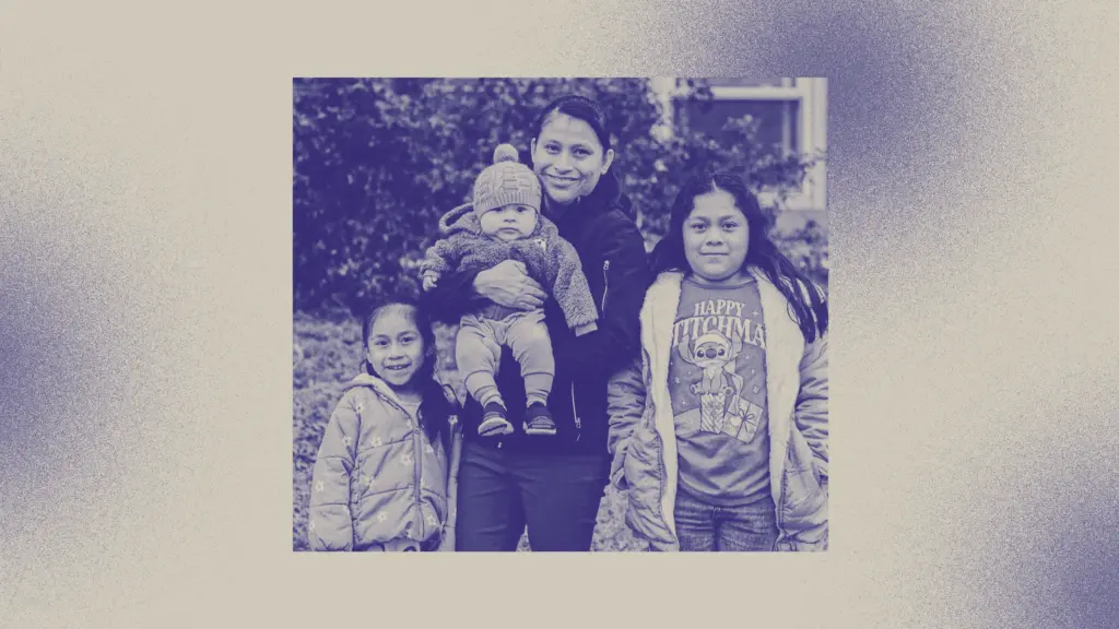 A young Guatemalan woman stands between two of her daughters holds the third, a baby. The family is smiling at the camera and the image has been treated with a purplish filter.