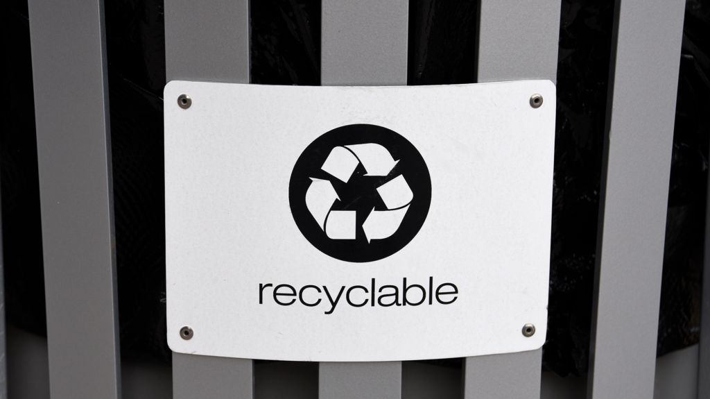 A white sign with the recycling symbol, three arrows pointing in a triangle, is above the word