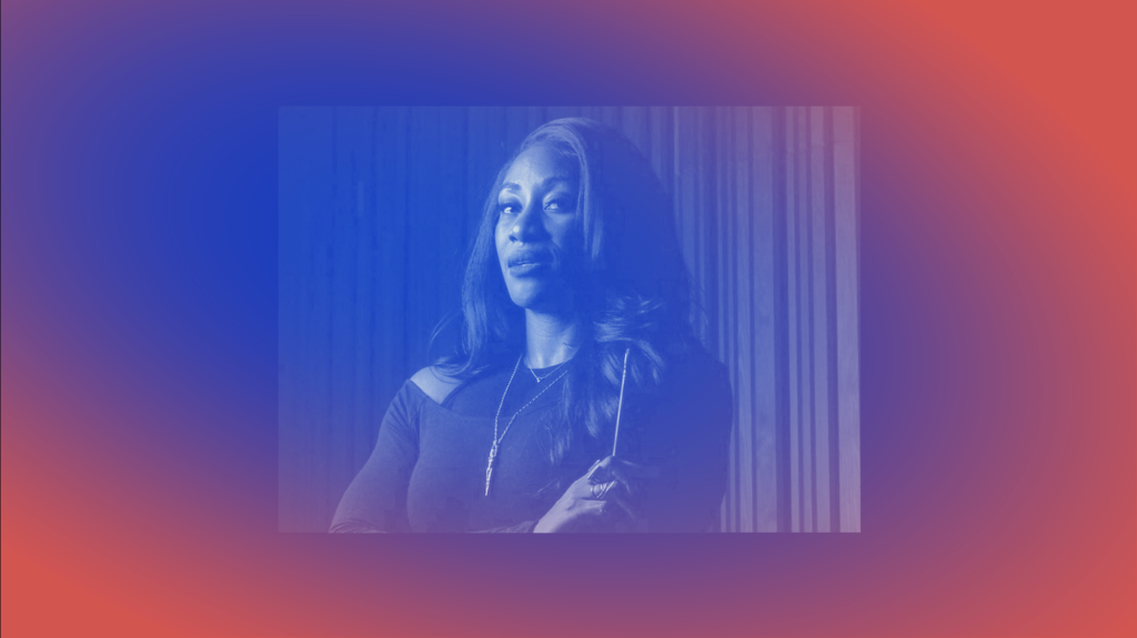 A portrait of a Black woman with long black hair looking into the camera with arms folded. She's wearing a black long-sleeve top and the photo is framed by a blue and red gradient.
