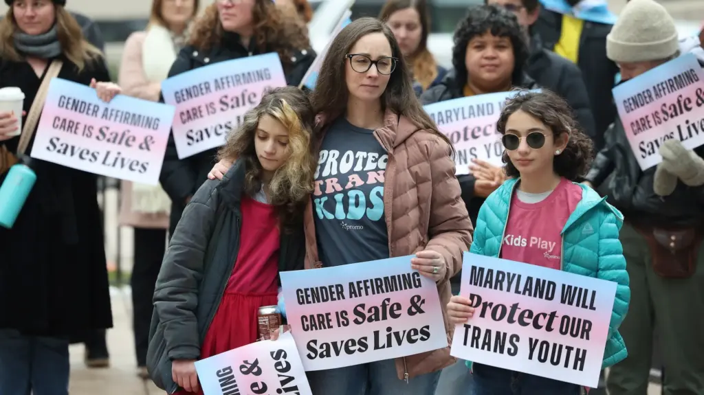 A woman and two children at a trans-rights protest look dejected as they hold signs saying 