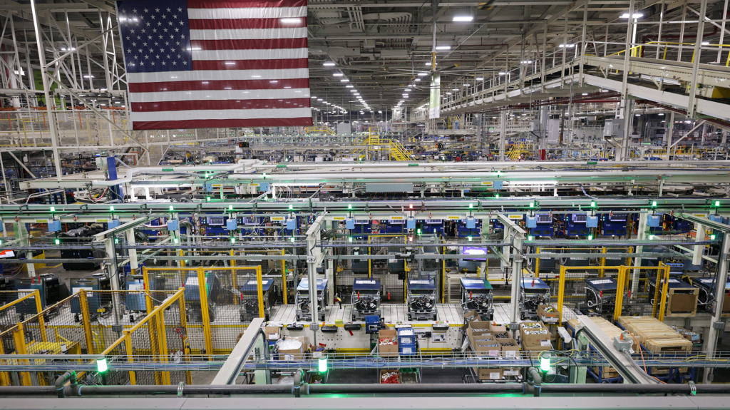 An American flag hangs over a brightly lit manufacturing facility.