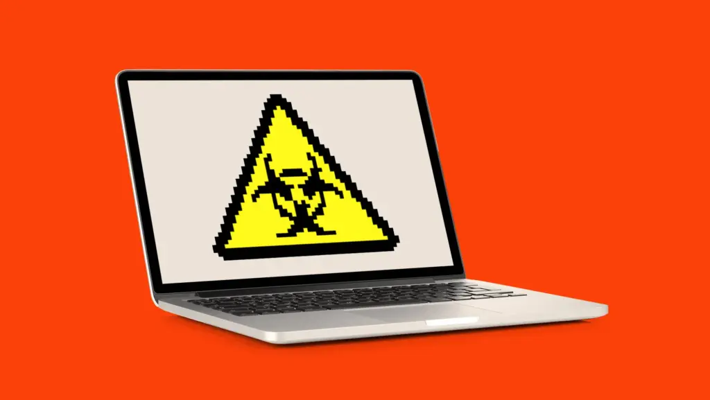 An open silver laptop against a solid orange background displays a pixelated yellow warning triangle containing a black biohazard symbol.