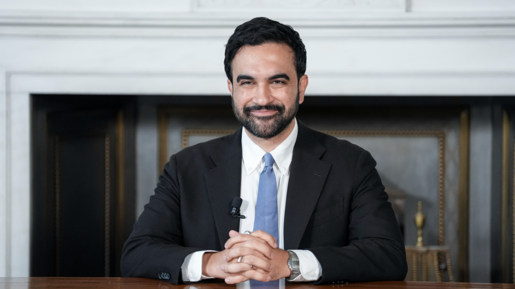 Zohran Mamdani sits in a suit.