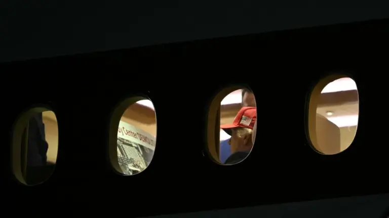 Photographed from the outside of a plane, Trump looks at a poster board that reads 
