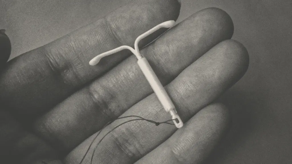 A black-and-white close-up photo of the fingers of a hand, on which lies a T-shaped birth control device known as an intrauterine device.