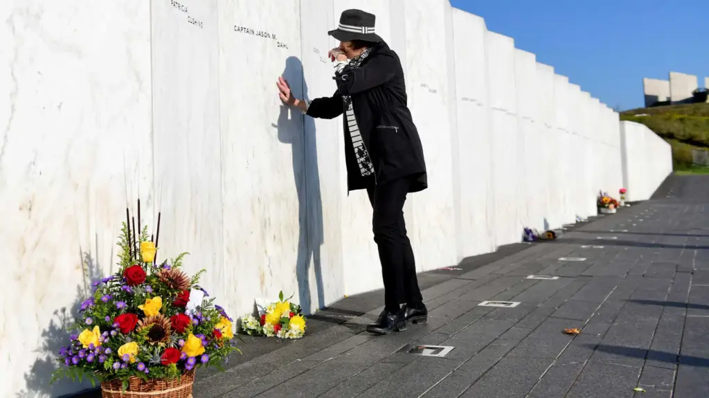 A woman holds her hand up to the Flight 93 wall of names.