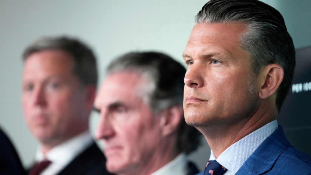 Three people are shown in a photo. From right to left:Defense Secretary Pete Hegseth, from right, Interior Secretary Doug Burgum, and Army Secretary Dan Driscoll. Driscoll and Burgum are blurred a bit as the photo is focused on Hegseth. All three are standing indoors.