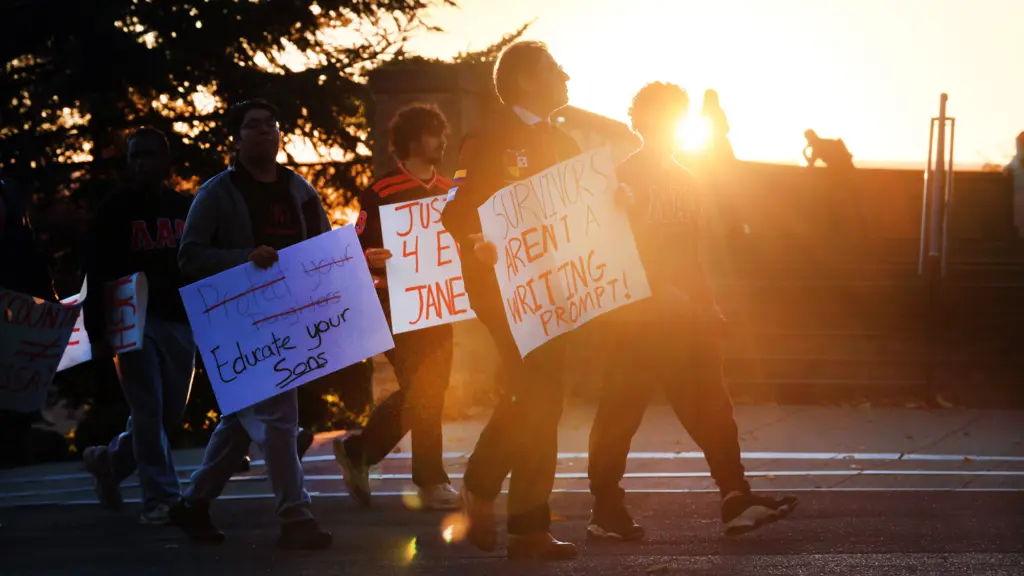A photograph of several young people with signs, seen in shadow against a setting sun. One person holds a sign that reads 