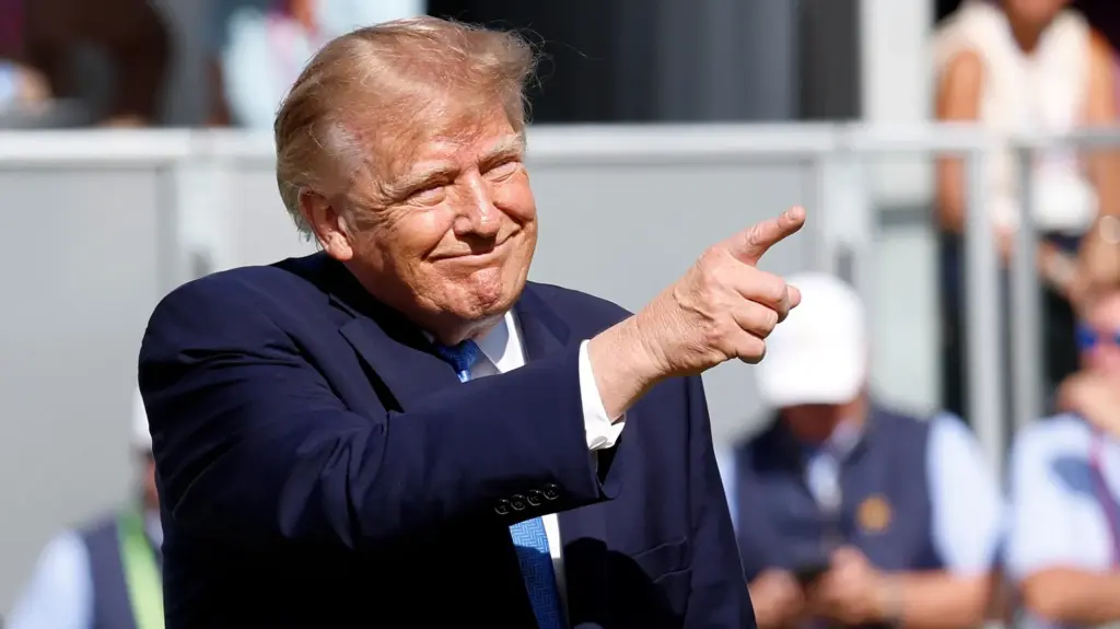 Donald Trump smiles and points on a sunny day.