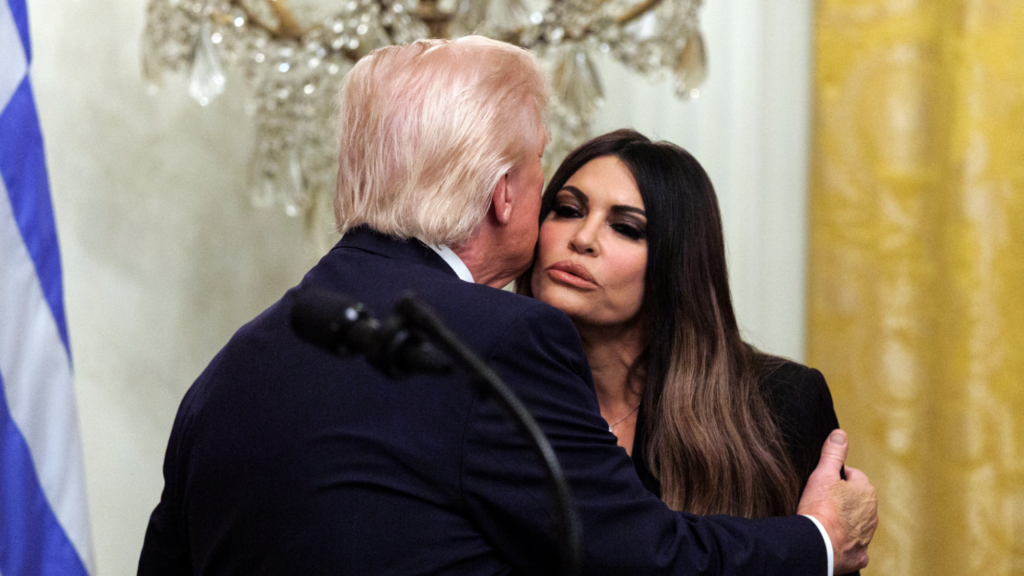 Photo of United States President Donald J Trump (L) and US Ambassador to Greece Kimberly Ann Guilfoyle (R), both wearing black, greet each other by cheek kissing at the White House. In the background is a white and gold wall and part of the Greece flag.